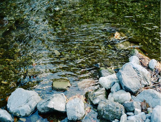 前景に岩と水が流れる川の風景。自然の美しさが感じられる静かなシーン